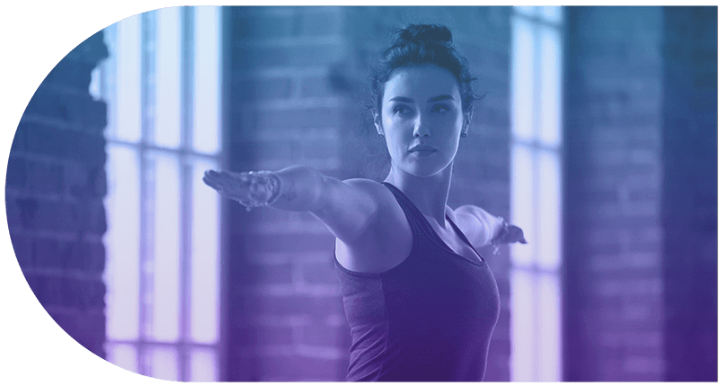 Woman stretching her arms in a gym with large windows and brick walls.