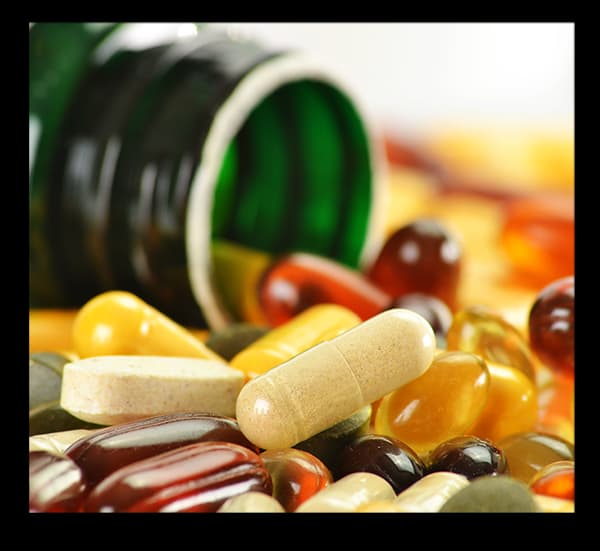 A green bottle tipped over with various colorful pills and capsules spilled out.