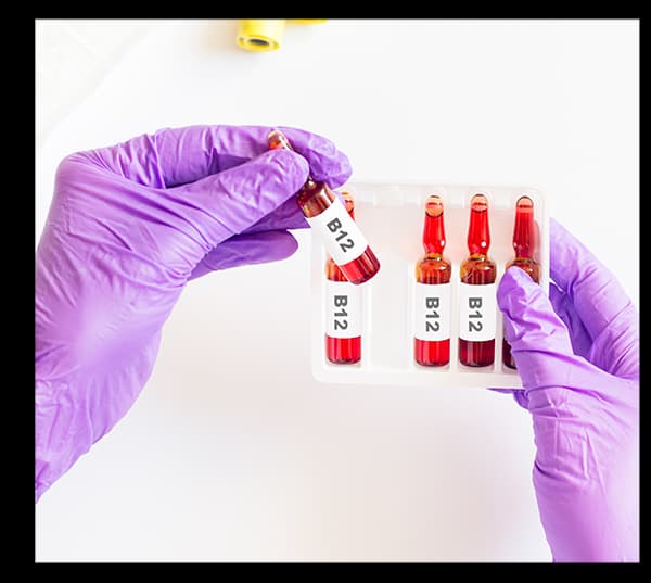 Person wearing purple gloves handling blood samples in vials labeled B12 in a laboratory setting.